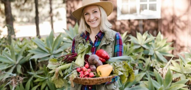 Smiling woman in a sun hat holding a basket of fresh produce